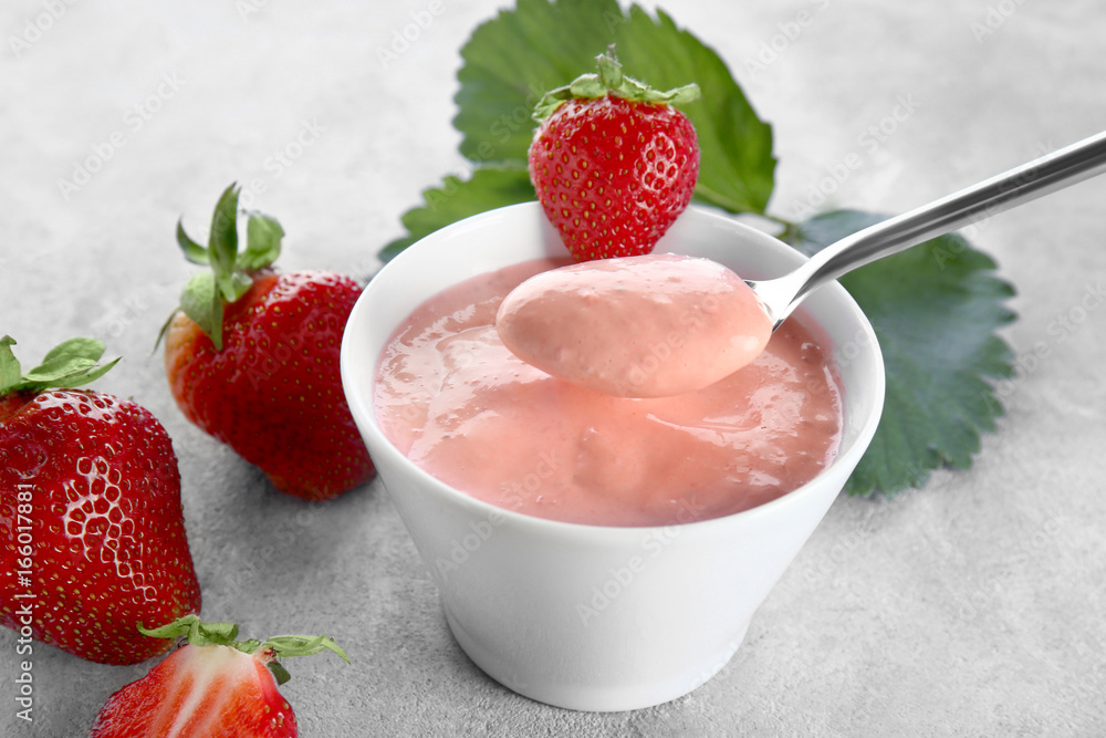 Composition of bowl and spoon with homemade strawberry yogurt on grey background Composition of bowl and spoon with homemade strawberry yogurt on grey background