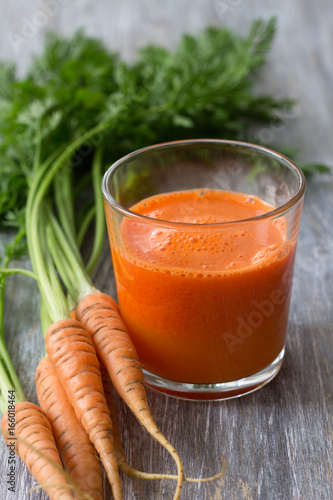 Freshly squeezed carrot juice from a young carrot in a glass on a wooden table, selective focus