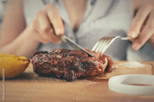 Woman eating delicious grilled steak on wooden board in restaurant