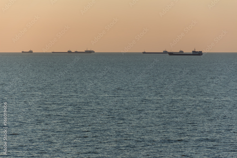 Trading ships or barges on the horizon of the sea during sunset or dawn.