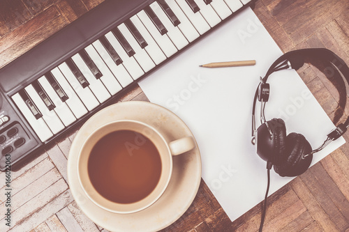 songwriter concept. piano, headphone, coffee cup, pencil & blank white paper on wooden floor photo