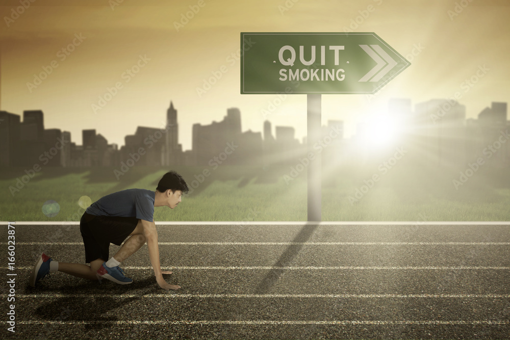 Male runner with quit smoking word on signpost Male runner with quit smoking word on signpost