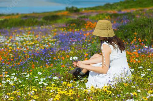 Young woman sitting in the sun in colourful wildflowers photo