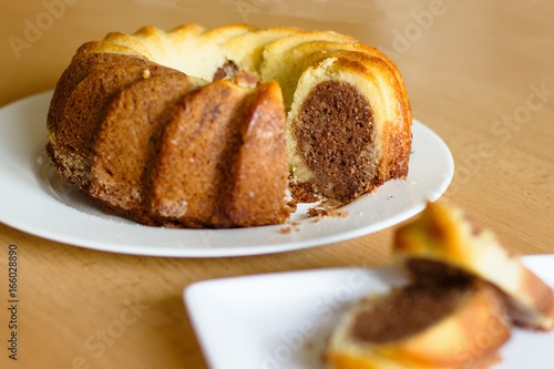 Traditional two color (marmor) madeira cake on wooden table, selective focus on the cake, served slices intentionally out of focus.