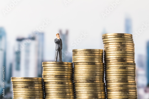 miniature model of investor standing on coin with city background. Business successful concept.