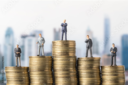 miniature model group of investor standing on coin with city background. Business successful concept.