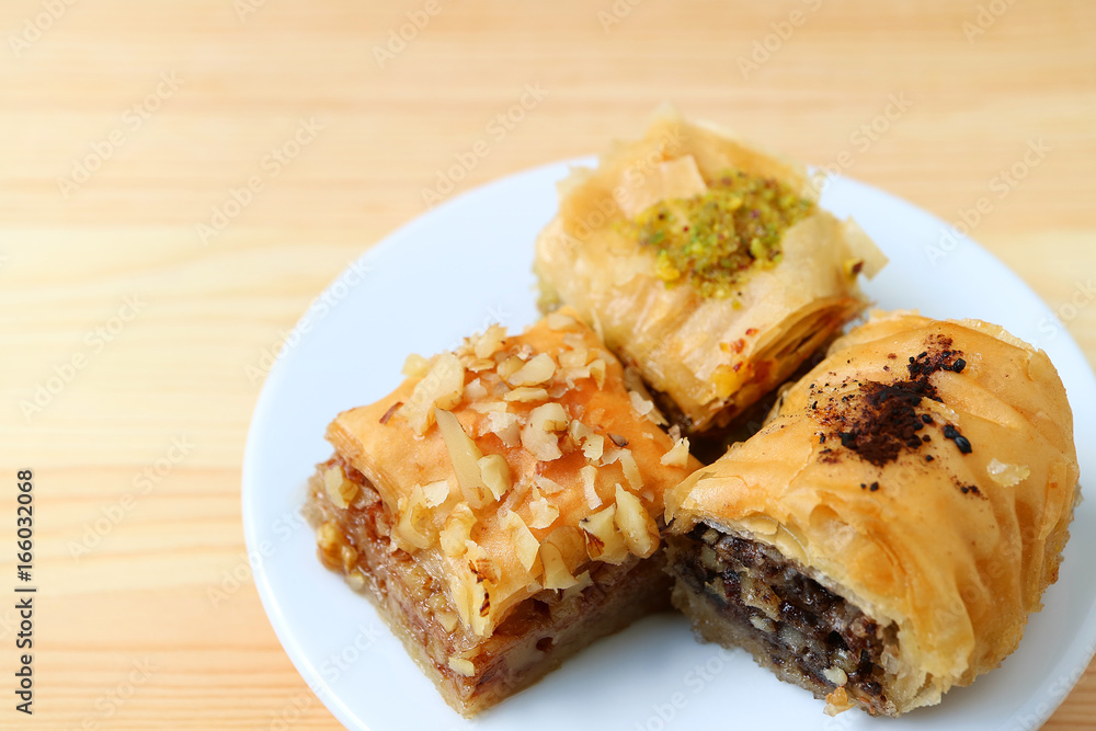 Plate of three types of Baklava sweets served on wooden table, selective focus with free space for text and design 