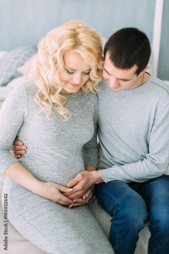Pregnant girl with her husband sitting on bed Pregnant girl with her husband sitting on bed