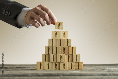 Bilde på lerret Businessman building a pyramid of wood blocks with people silhouettes