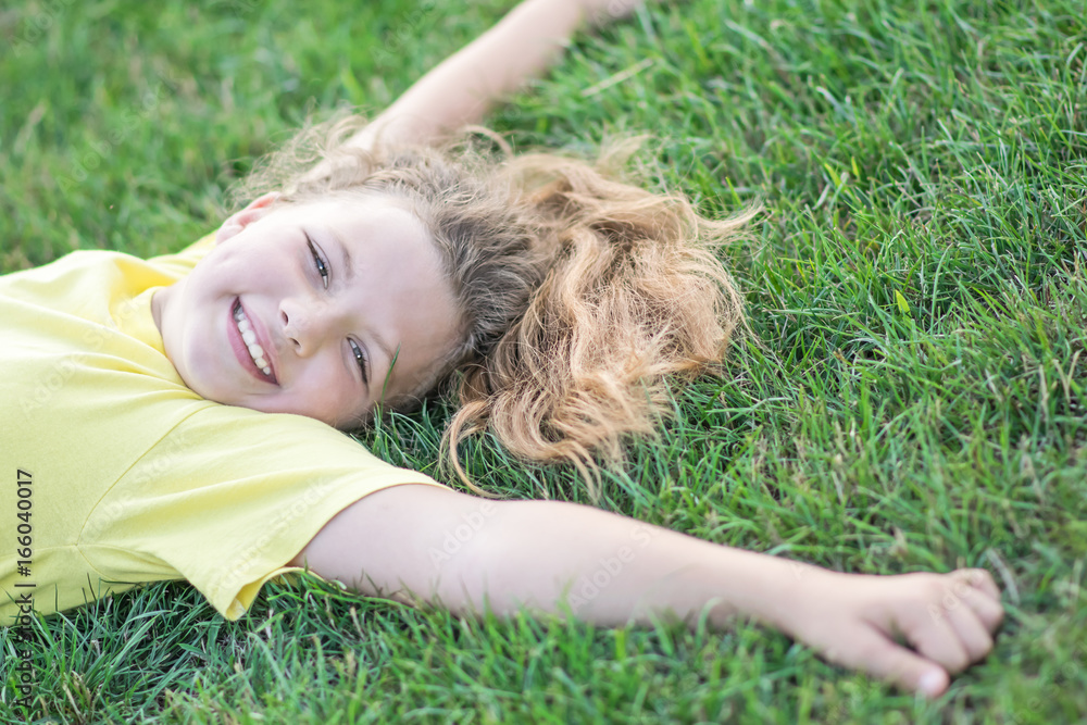 Happy pretty girl lying on green grass with outstretched arms and smiling at summer Happy pretty girl lying on green grass with outstretched arms and smiling at summer