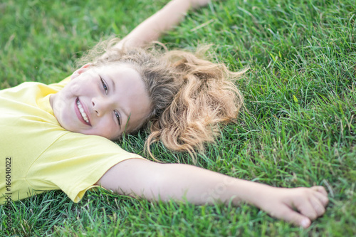 Happy pretty girl lying on green grass with outstretched arms and smiling at summer