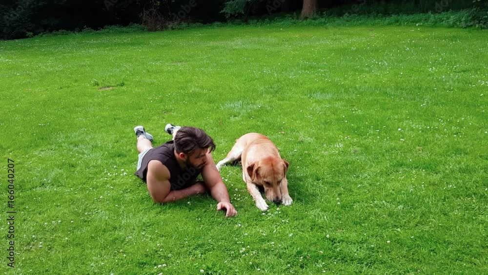 Junger Mann in Sport Outfit liegt im Park und spielt mit seinem Hund, Labrador