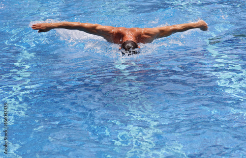 Strong muscular man swimming in pool butterfly style. Active summer holiday vacation. Sport, healthy lifestyle concept