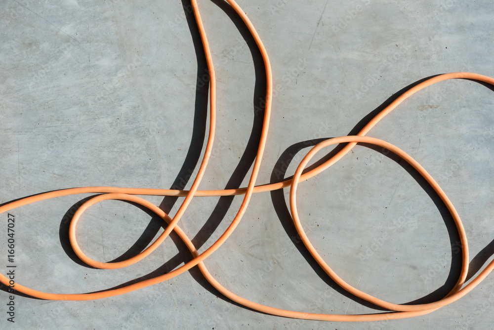 Abstract background - high angle view of orange electrical cord on concrete background with strong shadows Abstract background - high angle view of orange electrical cord on concrete background with strong shadows