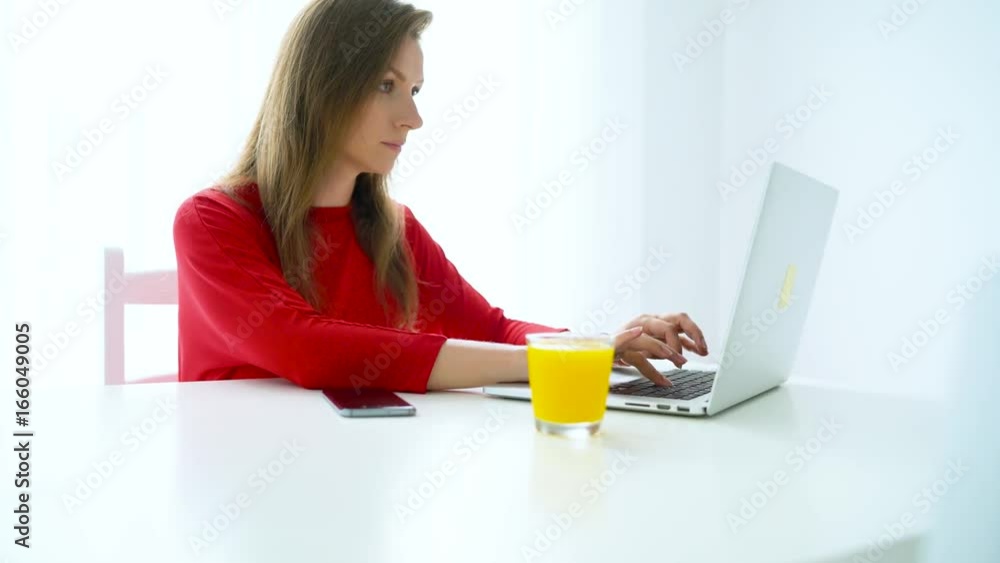 Smiling woman sitting at white home office and working on a laptop Smiling woman sitting at white home office and working on a laptop