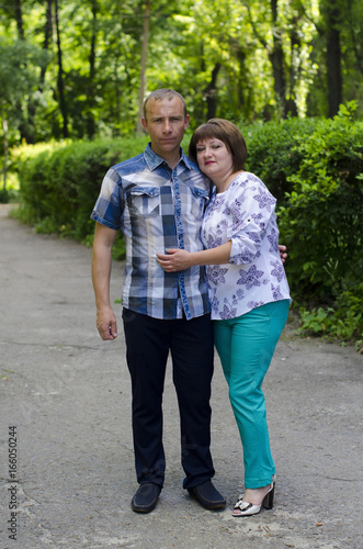  A happy married couple are standing in an embrace against the background of a green fence from a bush.