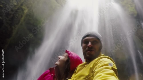 Young happy traveling couple taking a selfie on gopro camera. Man and woman near the Gljufrabui waterfall in Iceland.