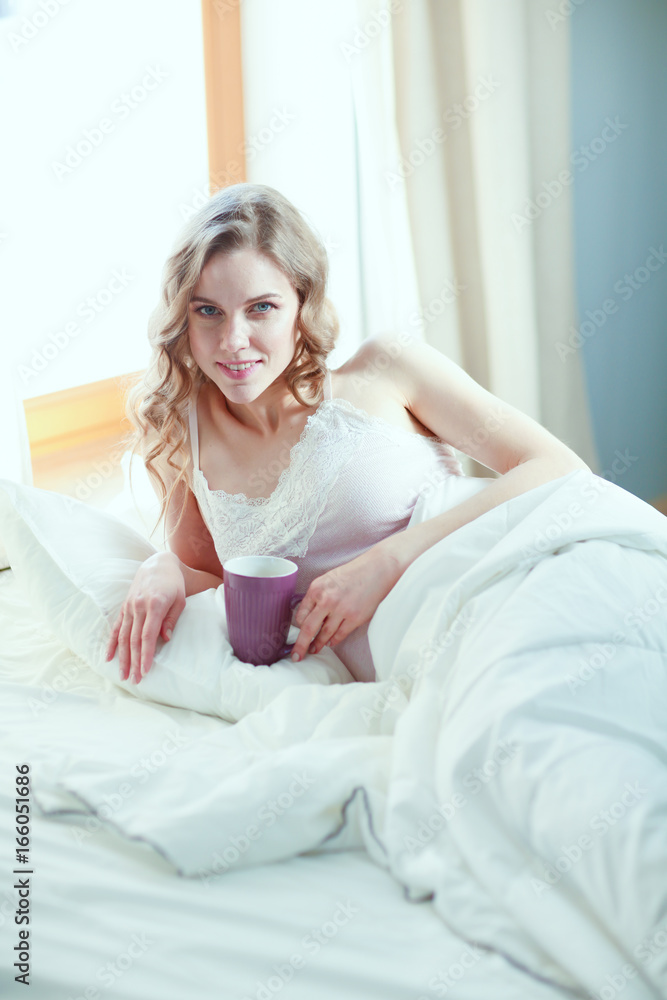 Young woman drinking cup of coffee or tea while lying in bed. Young woman drinking cup of coffee or tea while lying in bed.