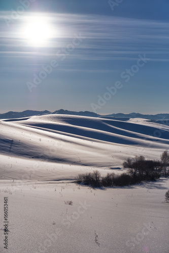 Winter landscape with heels under snow with Sun on blue sky
