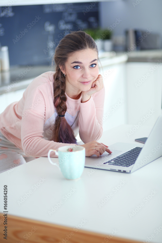 Young woman sits at the kitchen table using a laptop and talking on a cell phone. Young woman sits at the kitchen table using a laptop and talking on a cell phone.