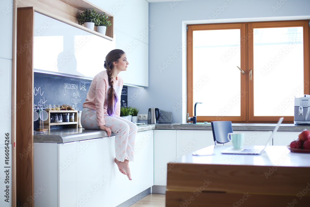 Young woman sitting on table in the kitchen. Young woman sitting on table in the kitchen.