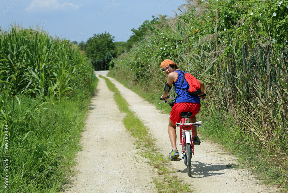 Fototapeta premium Young cyclist pedal on road with side corn fields in summer