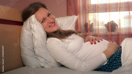 Young happy pregnant woman caress her abdomen belly and look into camera