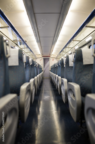 Empty interior of a passenger train car aka coach or carriage . Rows of unoccupied seats and folding tables in economy or second class.