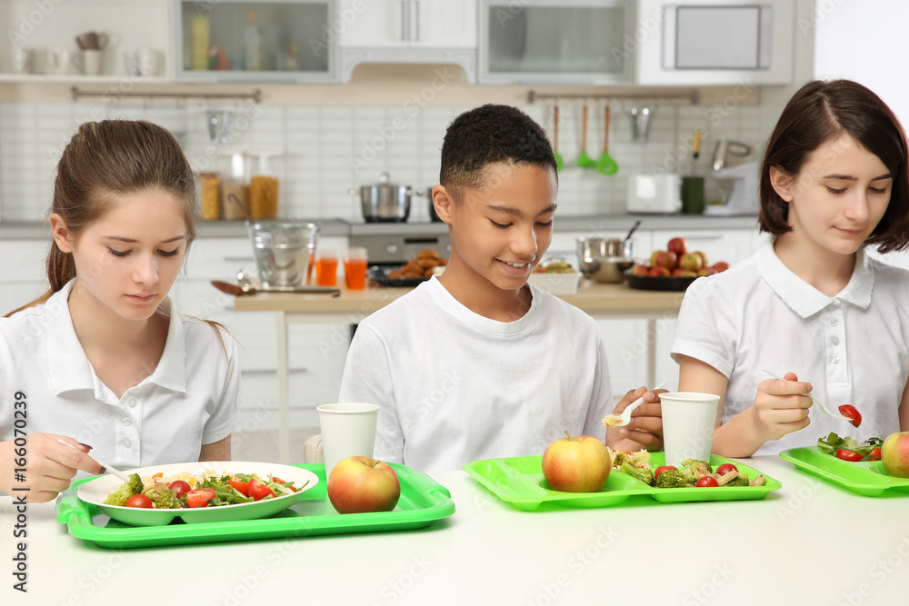 Children sitting at table in school cafeteria while eating lunch Children sitting at table in school cafeteria while eating lunch
