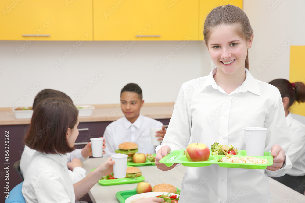 Cute girl holding tray with delicious food in school canteen