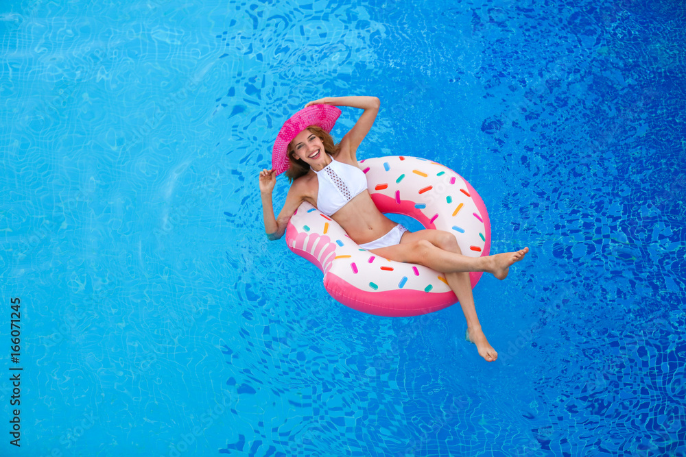 Beautiful young woman and inflatable donut in blue swimming pool