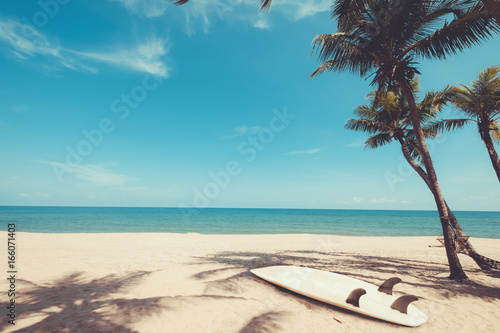 Fototapeta Naklejka Na Ścianę i Meble -  Surfboard on tropical beach in summer. landscape of summer beach and palm tree with sea, blue sky background. Vintage color tone