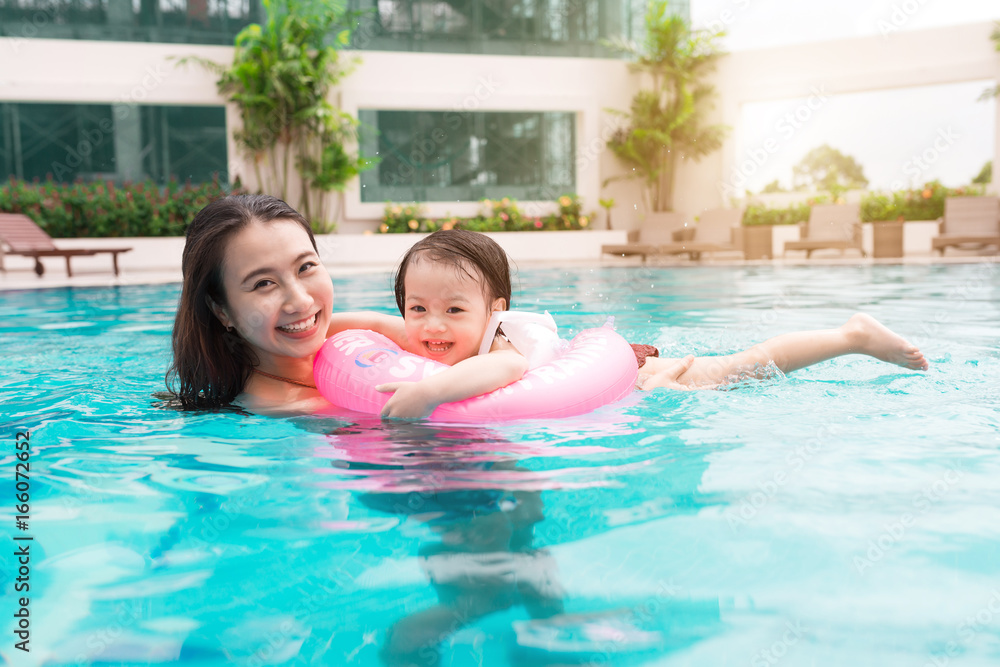 Mother and baby girl having fun in the pool. Summer holidays and vacation concept