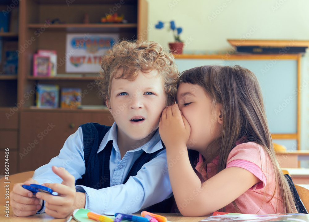 Fototapeta premium Girl telling secret to surprised boy in classroom.