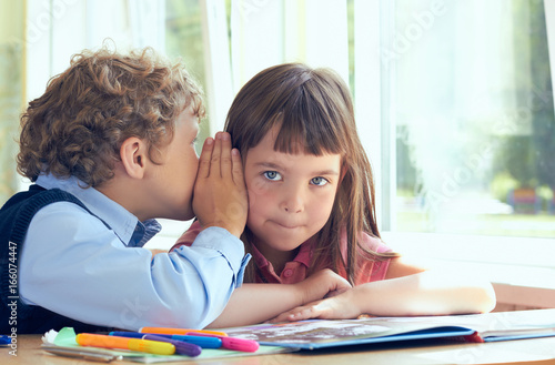 Happy boy whispering a secret in girls ear in school