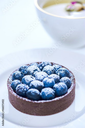 Hand made dessert tarlets from pistachio and chocolaty bakery dough with blueberry decoration served on plate with cap of tea photo