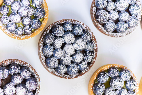 Hand made tarlets dessert from pistachio and chocolaty bakery dough with blueberry decoration on white background photo