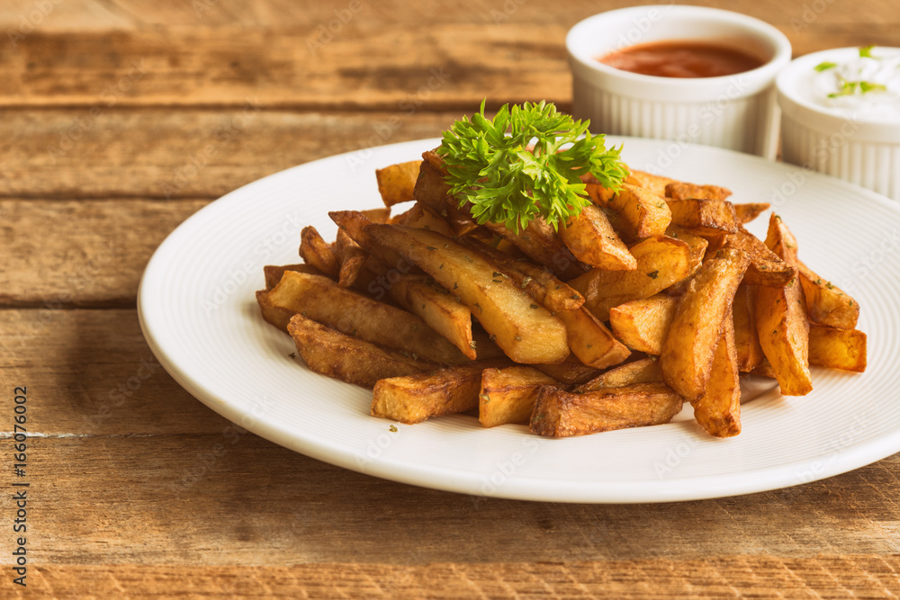 Homemade french fries serve with ketchup and sour cream or mayonnaise. Golden brown crispy french fries sprinkle with salt and oregano on white plate for snack or appetizer.French fries on wood table.