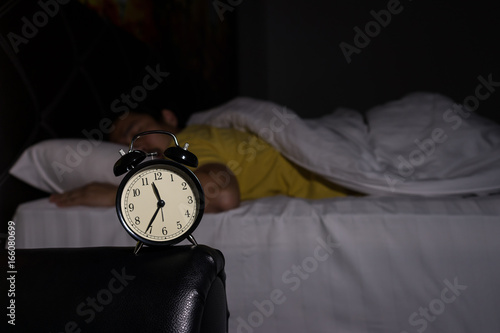 Alarm clock at 11:35 pm on bedside table in bed male sleeping in background, man rest in dark room at night