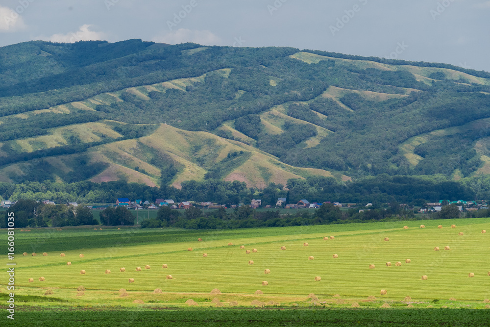 Beautiful landscape of a field with hay bales against the big hill