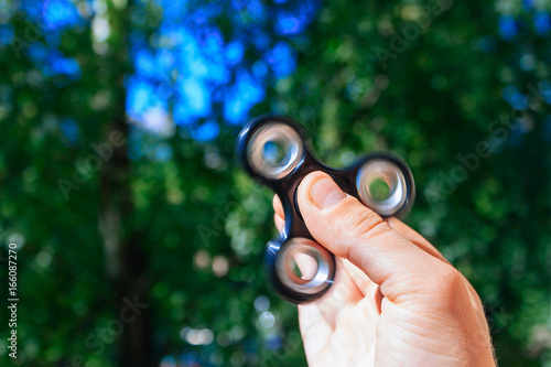 Hand with black steel rolling spinner. Green bokeh background.
