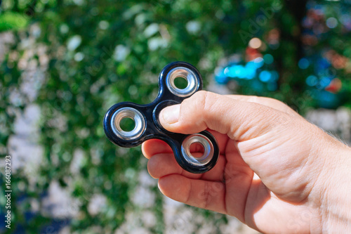 Hand with black steel rolling spinner. Green bokeh background.