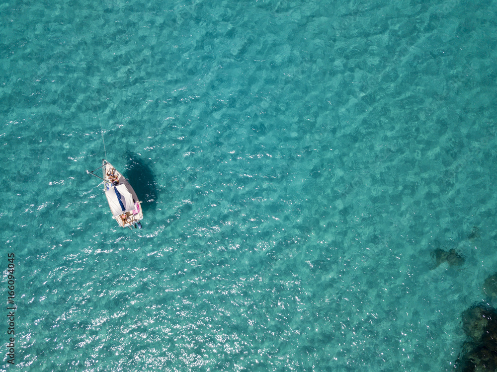 Vista aerea di una barca ormeggiata che galleggia su un mare trasparente. Immersioni relax e vacanze estive. Coste italiane, spiagge e rocce