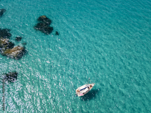 Vista aerea di una barca ormeggiata che galleggia su un mare trasparente. Immersioni relax e vacanze estive. Coste italiane, spiagge e rocce © Naeblys