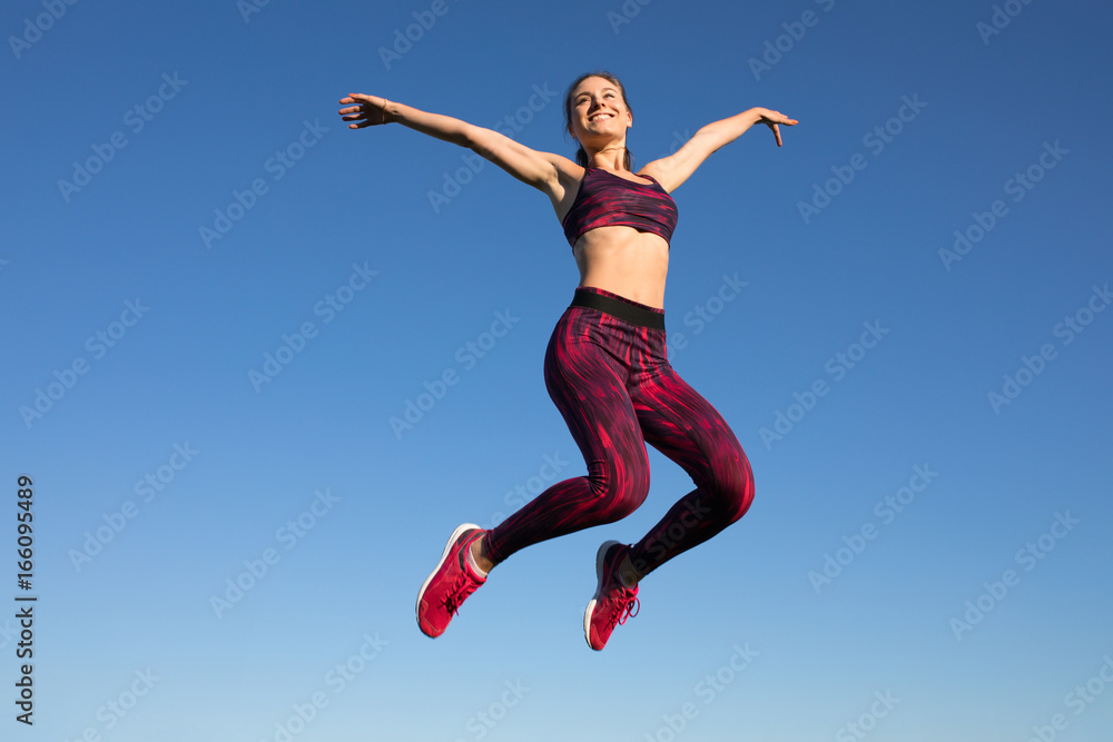 Isolated of young happy sportswoman in sportswear jumping and flying at blue sky background. She enjoying summer. Healthy lifestyle concept, sport activity.