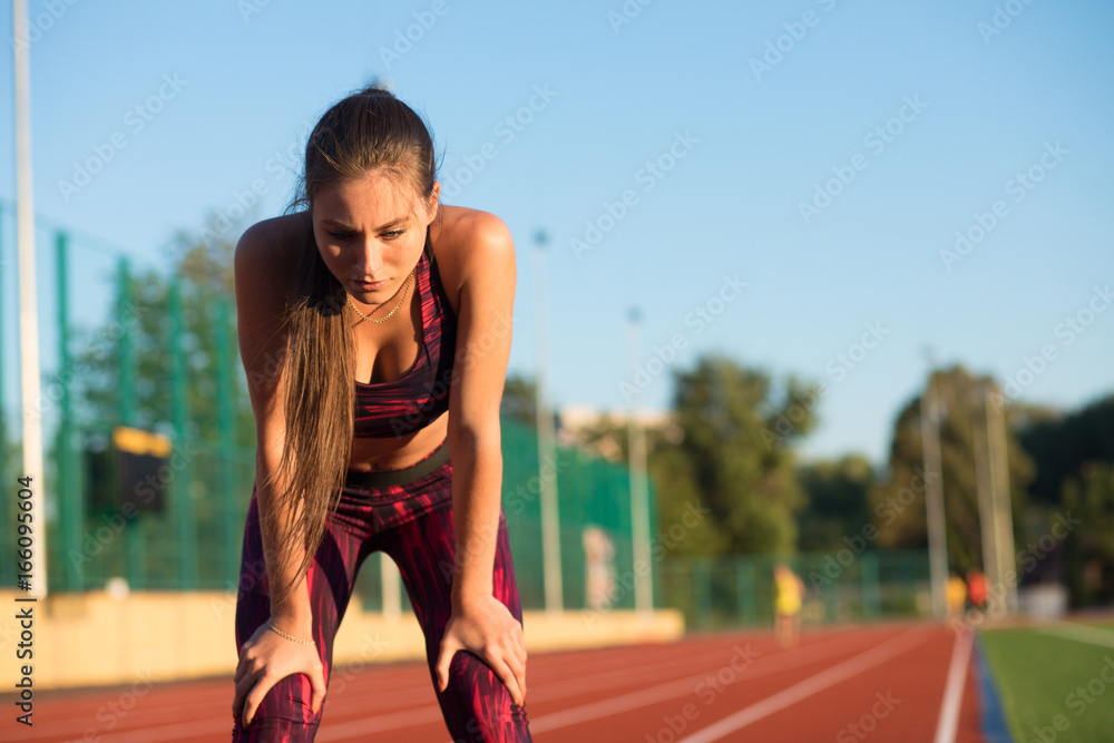 Young woman standing bent over and catching her breath during a running session Young woman standing bent over and catching her breath during a running session
