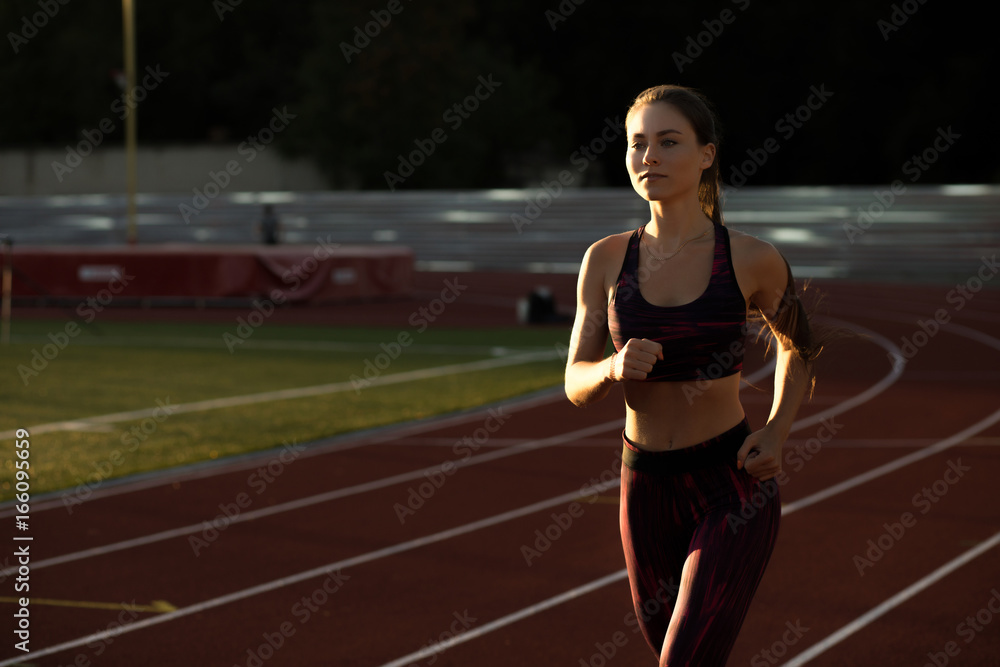 Obraz premium Professional sportswoman running outdoors at sunset. Female athlete in sportswear on stadium outdoors. Workout sport activity.