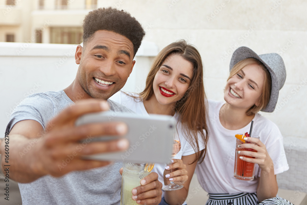 Multiethnic friends spending time togeher making selfie with cell phoe holding glasses with wine