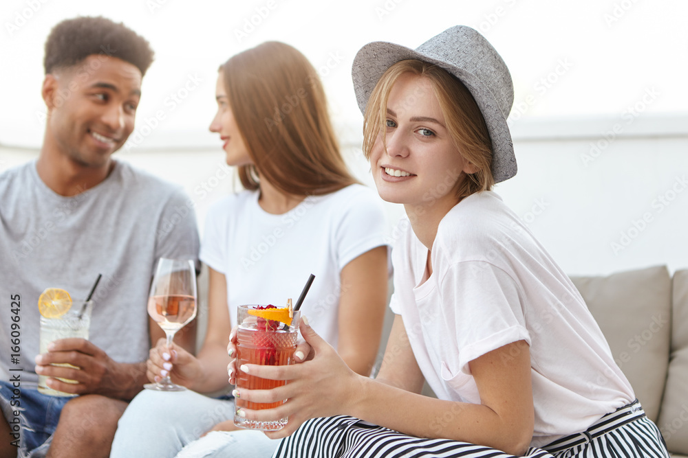 Portrait of youngsters sitting together at cozy sofa, drinking cocktails and wine having party. Mixed race people communicating with each other toasting by glasses. People, celebration, party concept Portrait of youngsters sitting together at cozy sofa, drinking cocktails and wine having party. Mixed race people communicating with each other toasting by glasses. People, celebration, party concept