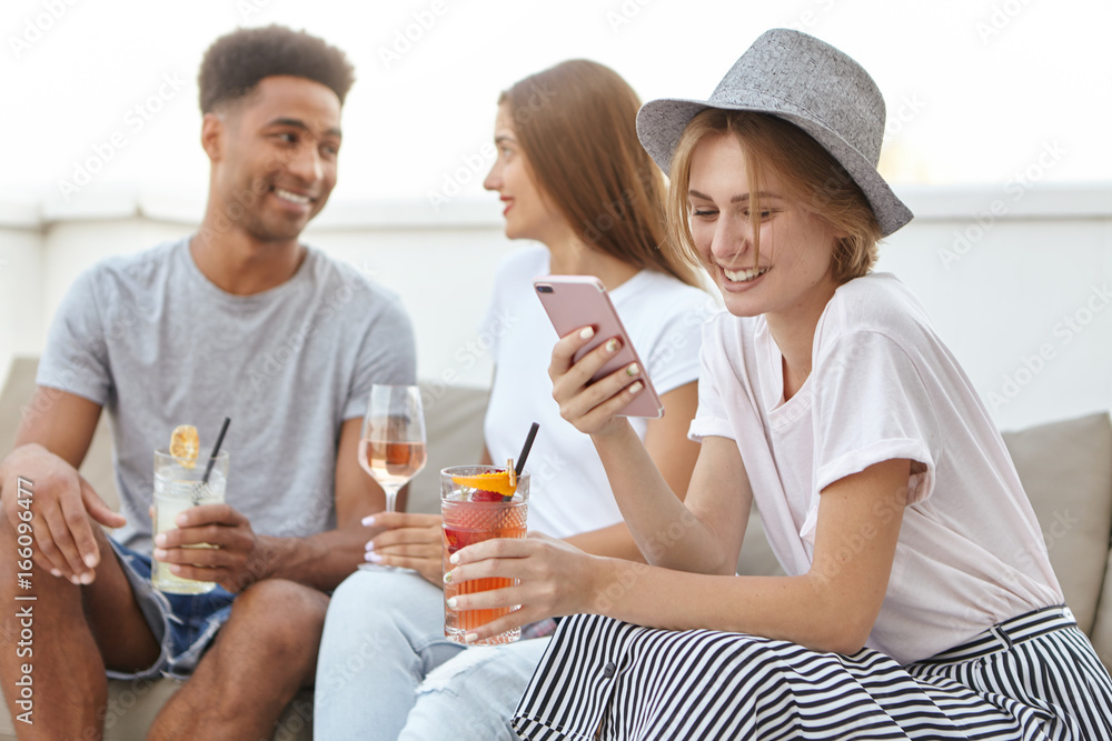 Glad female wearing hat and elegant clothes receiving message from her lover, spending time together with her colleagues, having corporative party, drinking alcoholic beverages. Friends, meeting Glad female wearing hat and elegant clothes receiving message from her lover, spending time together with her colleagues, having corporative party, drinking alcoholic beverages. Friends, meeting